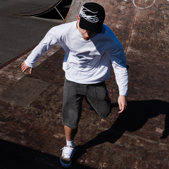 FROST mens 240 GSM heavyweight white longsleeve with cursive arm print, worn at UK skate park — overhead shot showing streetwear clothing fit